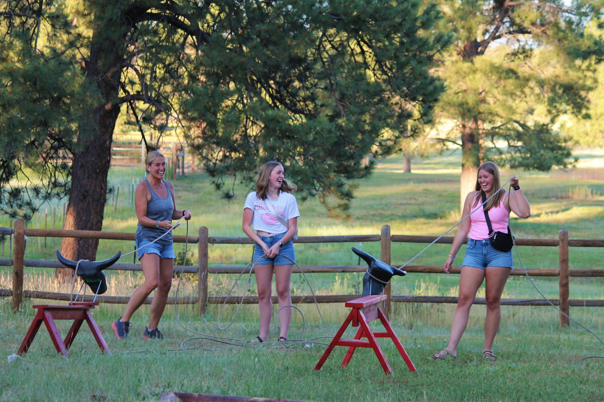 Three women smile and laugh as they throw ropes at pretend cows