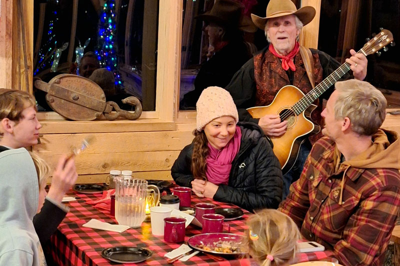 A family is serenaded by a cowboy playing the guitar at dinner